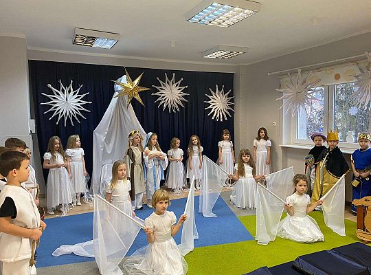 Dziewczynki ubrane  w białe sukienki klęczą trzymając białe flagi