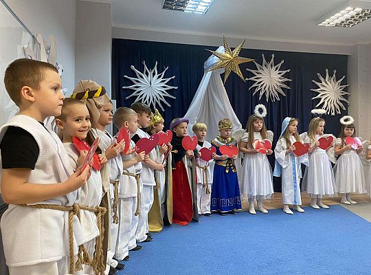 Dzieci trzymając przed sobą serduszka śpiewają