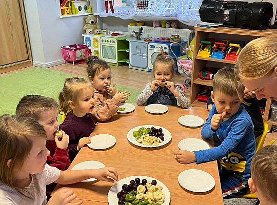 Dzieci przy wspólnym stole jedzą urodzinowe owoce