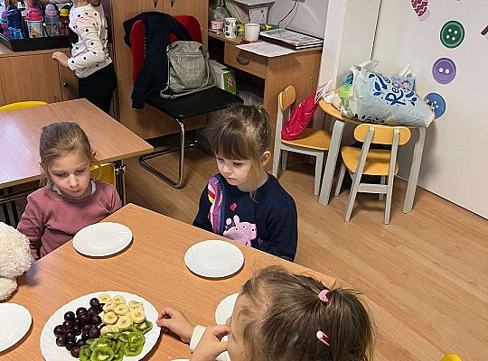 Dzieci przy wspólnym stole jedzą urodzinowe owoce