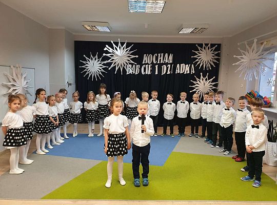 Chłopiec mówi wierszyk a  dziewczynka stoi obok niego, w otoczeniu grupy