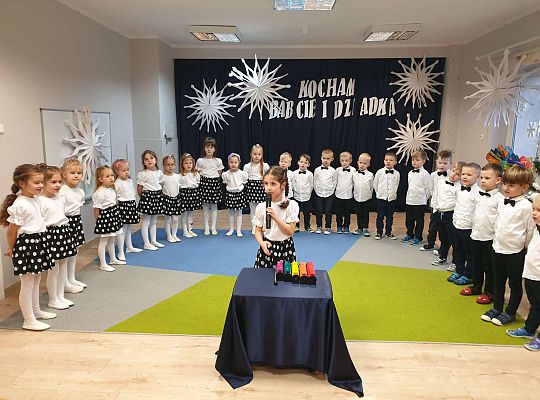 Dziewczynka śpiewa piosenkę przez mikrofon przed nią cymbałki a w tle grupa dzieci