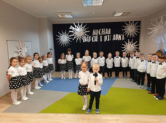 Chłopiec mówi wiersz a dziewczynka stoi obok niego na tle grupy