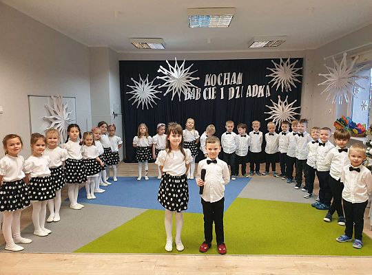 Chłopiec mówi wiersz a dziewczynka stoi obok niego na tle grupy