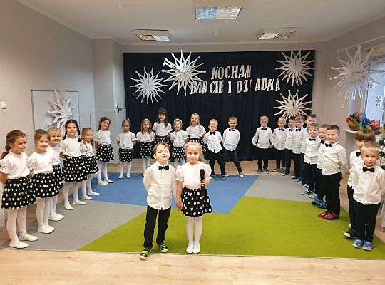 Dziewczynka mówi wiersz a chłopiec stoi obok na tle grupy