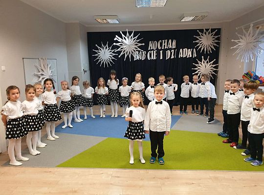 Dziewczynka mówi wiersz a chłopiec stoi obok na tle grupy