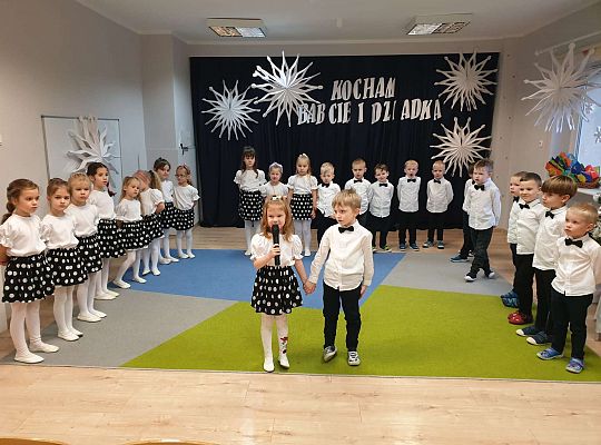 Dziewczynka mówi wiersz a chłopiec stoi obok na tle grupy