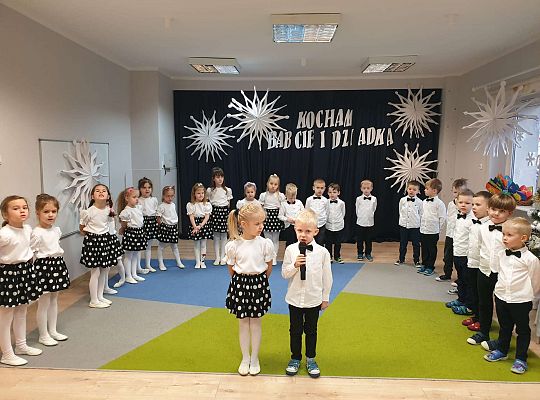 Chłopiec mówi wiersz a dziewczynka stoi obok niego na tle grupy