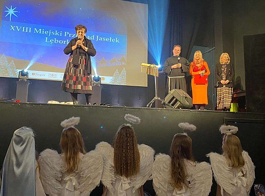 Dzieci przed sceną obserwują przemawiąjącą kobietę