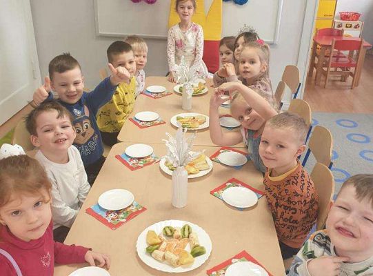 Dzieci siedzą z jubilatką przy wspólnym stole