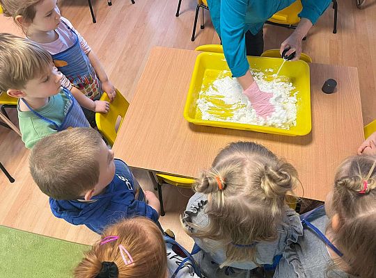 Pani pokazuje przedszkolakom jak ugniatać sztuczny śnieg
