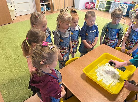Pani pokazuje przedszkolakom jak ugniatać sztuczny śnieg