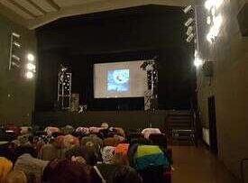 Dzieci siedzą w fotelach i oglądają przedstawienie