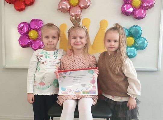 Natalka siedzi z albumem urodzinowym a obok niej stoją dwie dziewczynki
