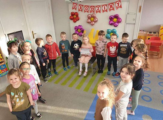 Natalka siedzi  z albumem urodzinowym a dookoła niej stoją dzieci