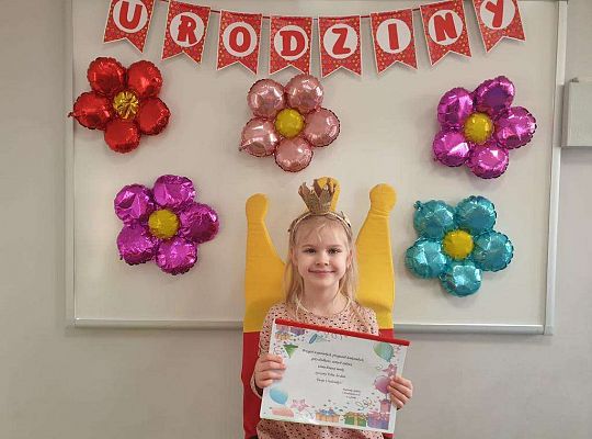 Natalka siedzi z albumem urodzinowym na tle dekoracji