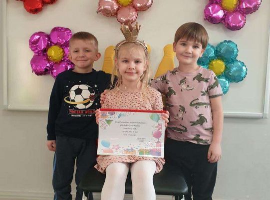 Solenizantka siedzi z albumem urodzinowym a obok niej stoją dwaj chłopcy