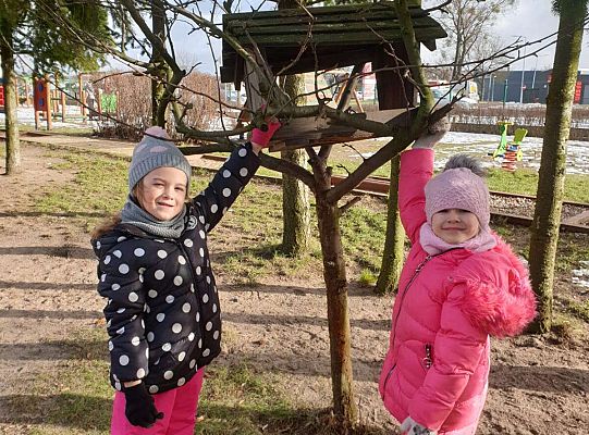Dwie dziewczynki zawieszają karmę dla ptaków przy karmiku