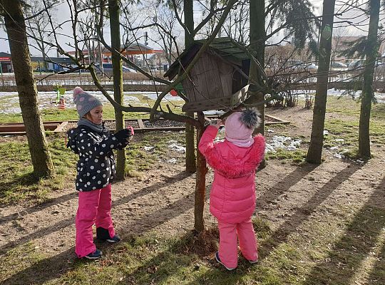 Dwie dziewczynki zawieszają karmę dla ptaków przy karmiku