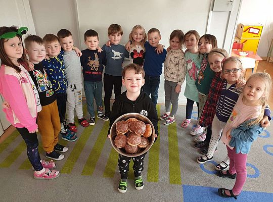 Chłopczyk trzyma miskę z pączkami a w koło niego stoją dzieci