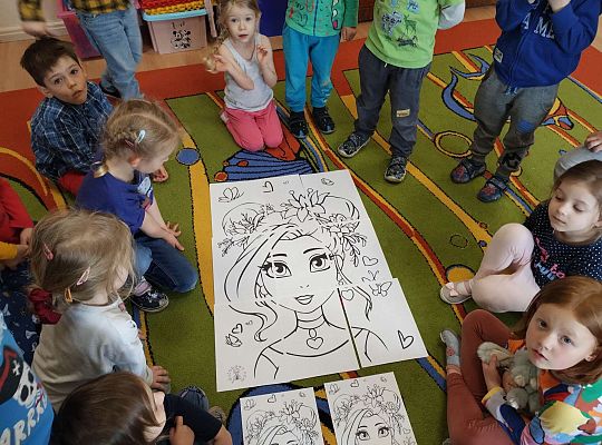 Dzieci słuchają instrukcji nauczyciela jak mają pokolorować Panią Wiosnę