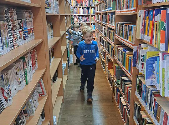 Dzieci idą między regałami z książeczkami
