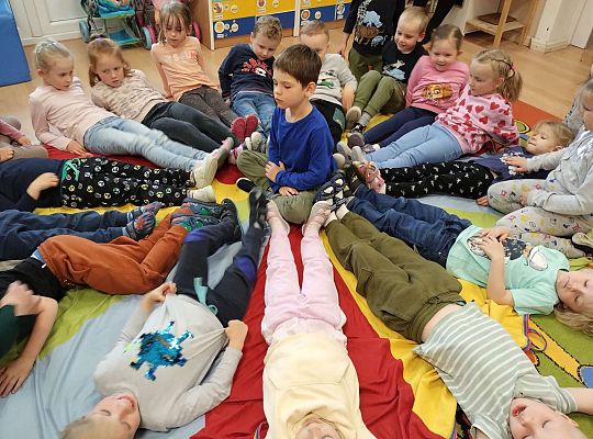 Chłopiec siedzi na środku chusty animacyjnej a dzieci wkoło